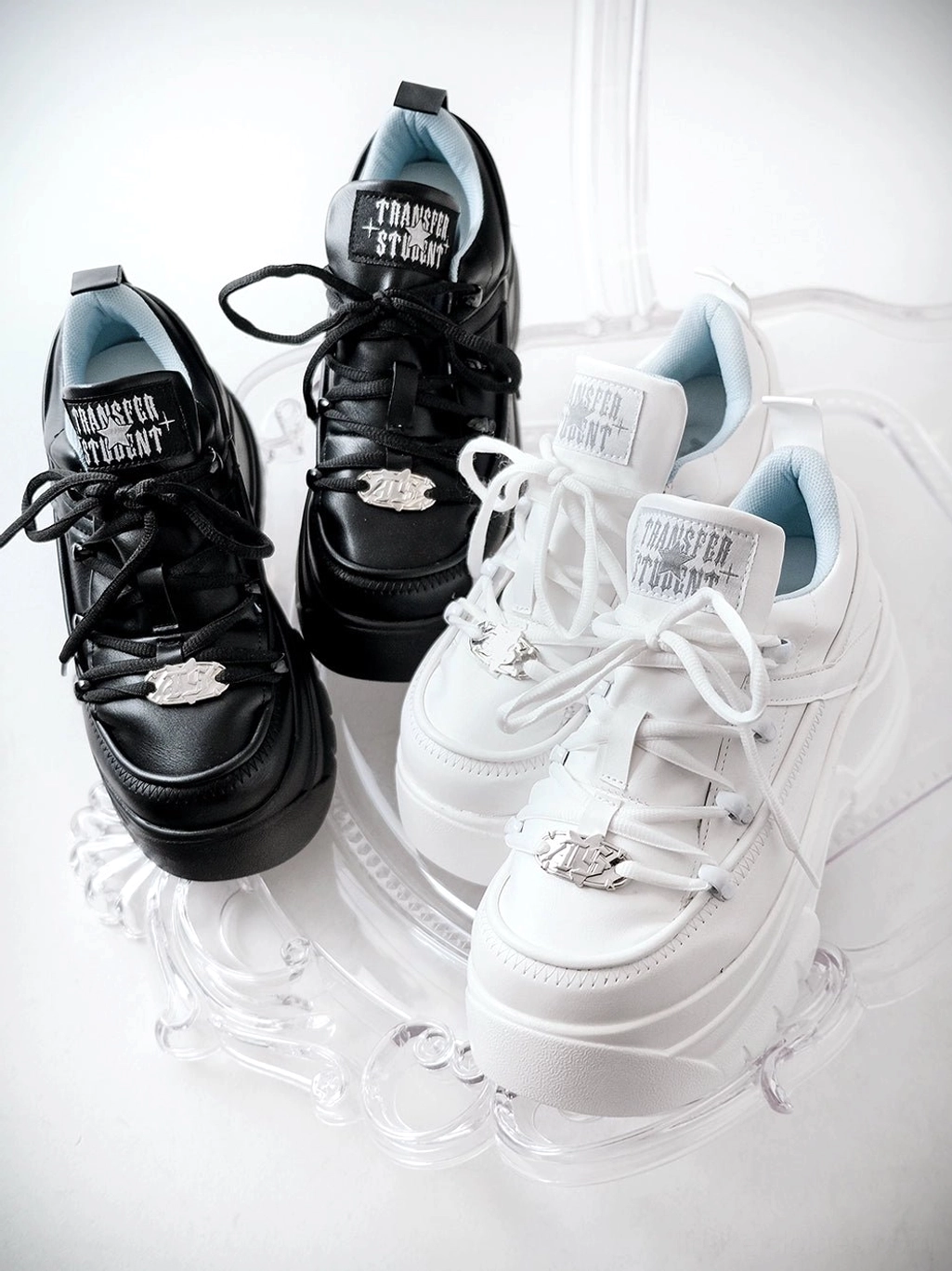 Black and white jirai kei platform sneakers top down flat lay view on clear acrylic stand showing chunky sole structure and metal hardware details