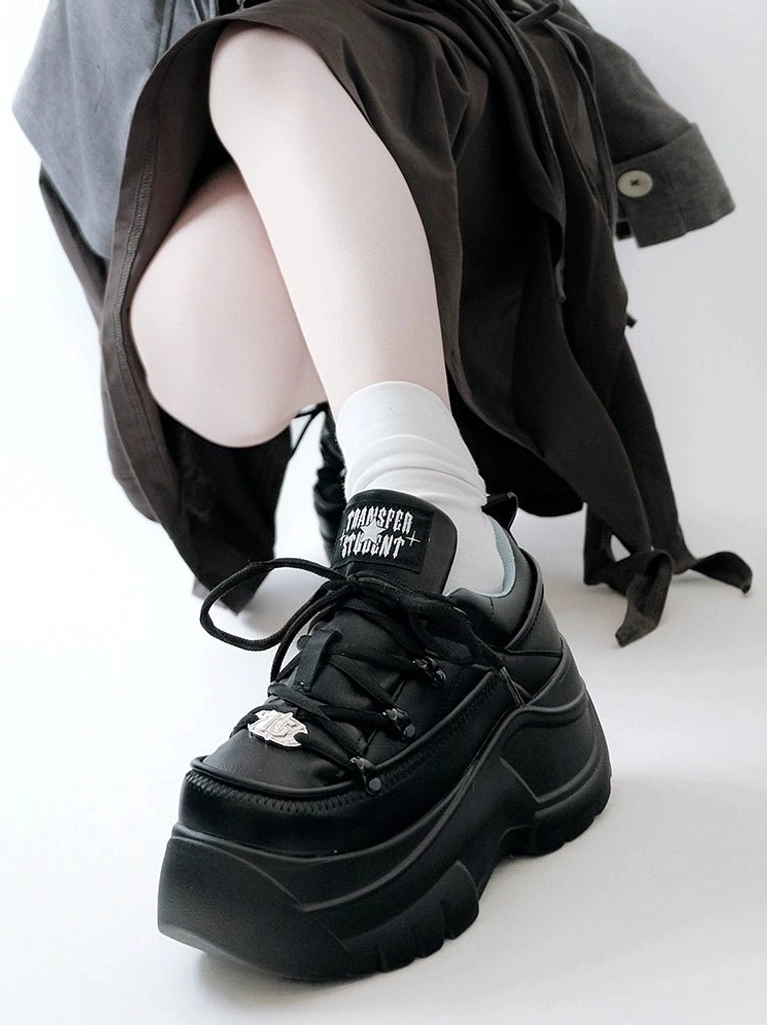 Black thick sole jirai kei platform sneakers seated model side view with loose outerwear and white socks showing 7cm back platform and branded tongue