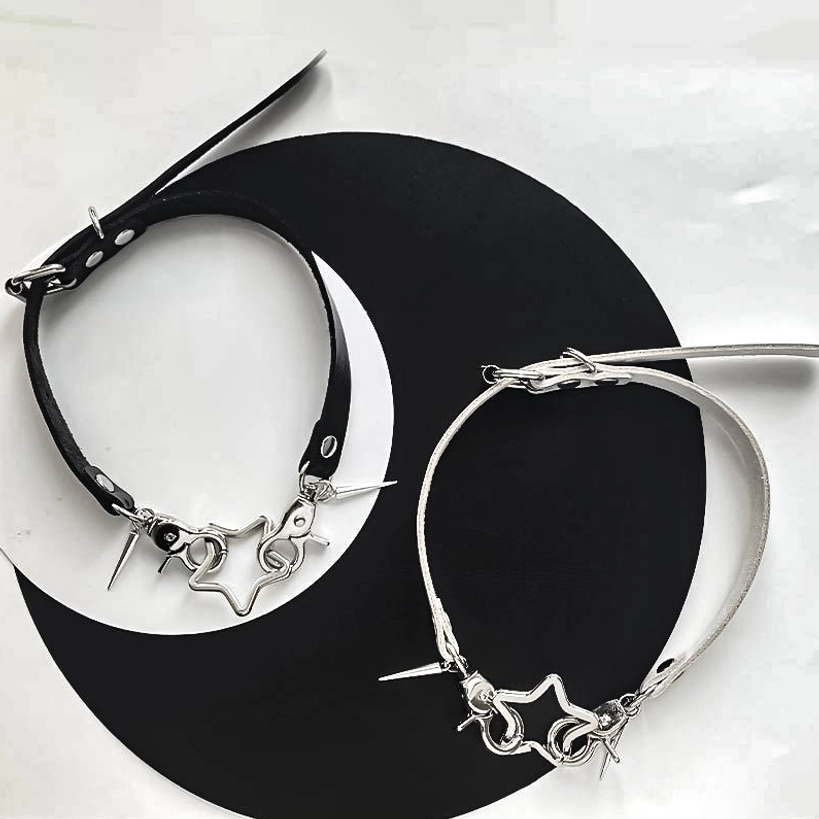 Black and white punk choker necklaces with star and spike hardware on crescent moon background flat lay display