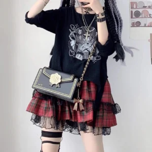 Rose-adorned black envelope jirai kei crossbody ita bag with gold chain strap worn with graphic tee and red plaid skirt