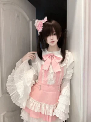 Jirai Kei Ryousangata suspender dress set with adjustable garter straps, pink and white lolita style salopette dress with ruffled lace trims and heart-shaped button accents, front half-body view on model with twin-tails hairstyle