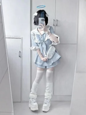 Model wearing light blue sailor Jirai Kei two-piece set with matching shorts, white thigh highs, and platform boots, paired with small crossbody bag in indoor wardrobe area