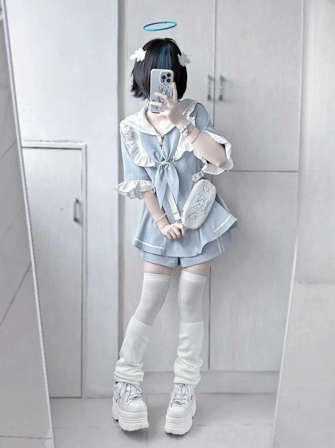 Model wearing light blue sailor Jirai Kei two-piece set with matching shorts, white thigh highs, and platform boots, paired with small crossbody bag in indoor wardrobe area