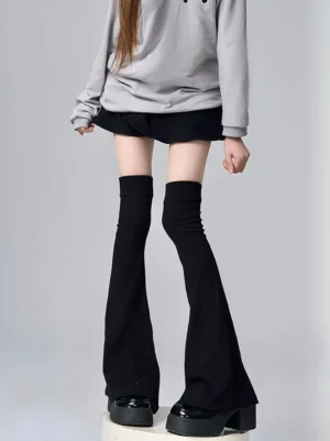 Solid matte black over-knee flared leg warmers front full leg view on female model in casual gray hoodie studio backdrop