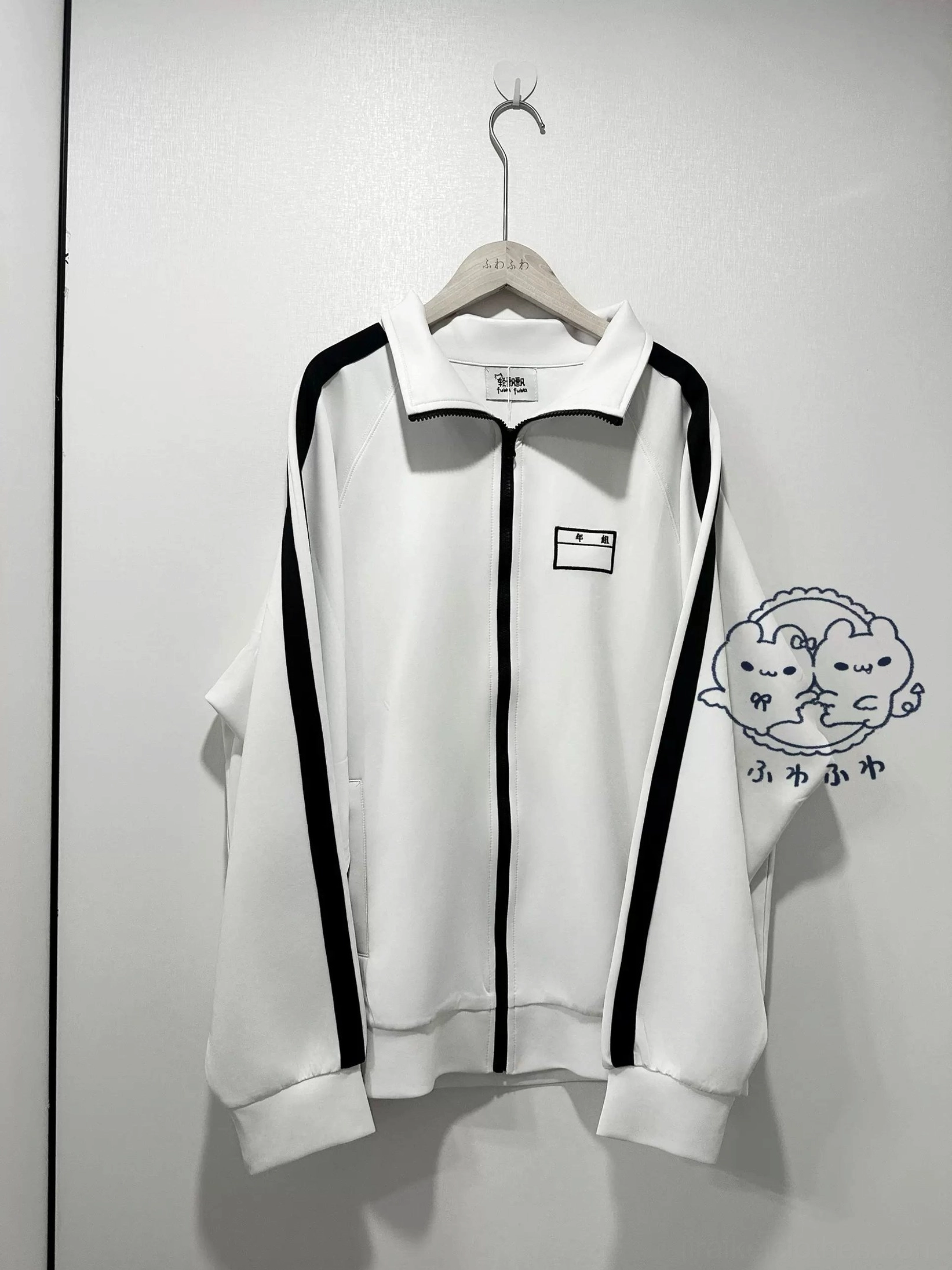 Black and white striped Jirai Kei sports jacket front detail view on flat lay, highlighting stand collar, full-length zipper placket with black stripe trim, chest embroidered patch design, and structured shoulder construction