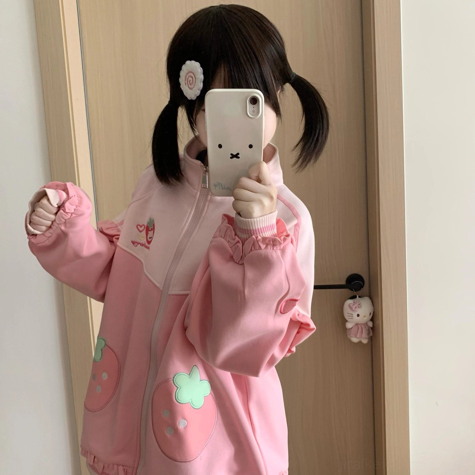 Side profile mirror selfie of Jirai Kei strawberry outfit worn by model with flower hair clip, highlighting ruffled sleeve details and loose-fit coat aesthetic