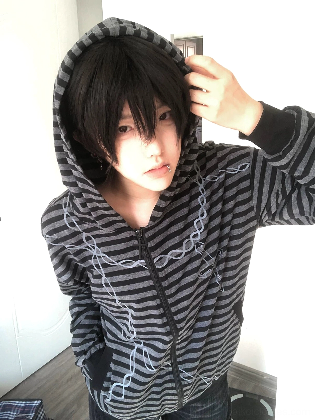 Gothic striped zip-up hoodie oversized fit half-body indoor view male model adjusting hood, displaying stripe and chain print details