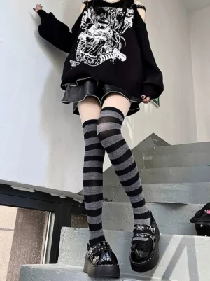 Female model wearing dark grey and black horizontally striped Jirai Kei over-the-knee socks, paired with punk-style outfit and platform shoes, shot in three-quarter view on indoor staircase