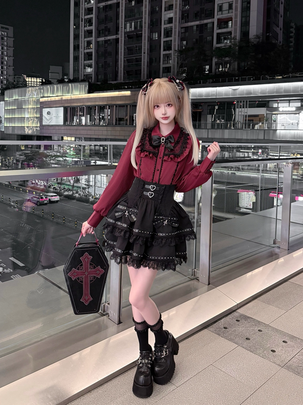 Three-quarter front view of Jirai Kei daily look featuring wine-red lace blouse with black tiered skirt, cross coffin bag, and platform boots on nighttime shopping terrace