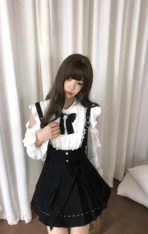 Jirai Kei two-piece outfit three-quarter view model posing with hand touching decorative chest bow pleated black skirt ruffled shirt details