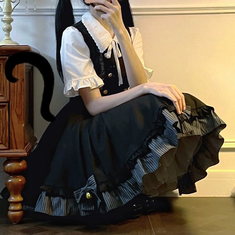 Side sitting angle view of complete Jirai Kei school uniform showing ruffled skirt hem with striped lining inside suspender skirt, wooden cabinet indoor wall background