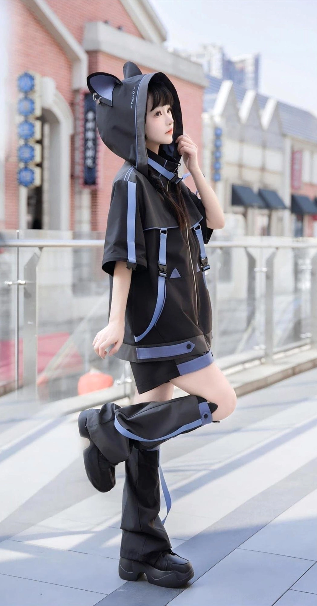Side pose with lifted leg showing cat ear hooded Jirai Kei jacket, matching leg warmers and shorts on urban street