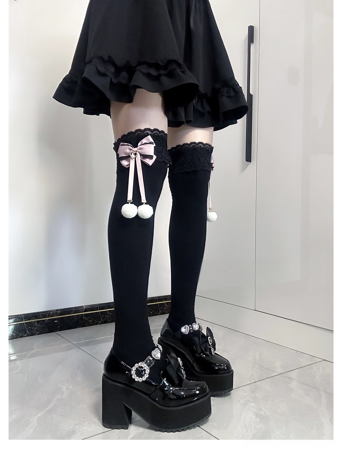 Jirai Kei thigh-high socks front-side partial leg view one sock featuring pink bow with white pom-pom another with plain lace cuff all-black fabric indoor styling