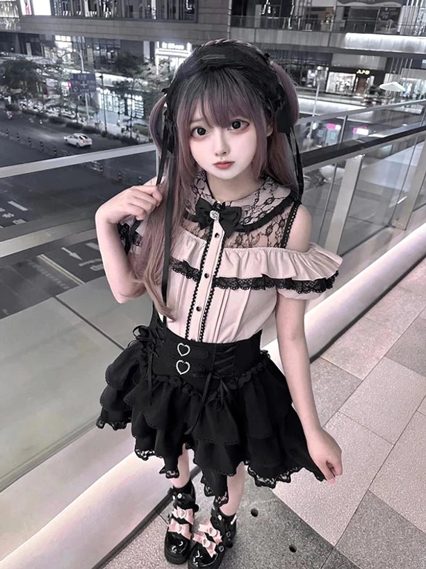 Low-angle front view of Jirai Kei two-piece set worn by model showing front buttoned blouse, heart-shaped waist buckles, lace-trimmed black tiered skirt hem, and romantic Gothic aesthetic