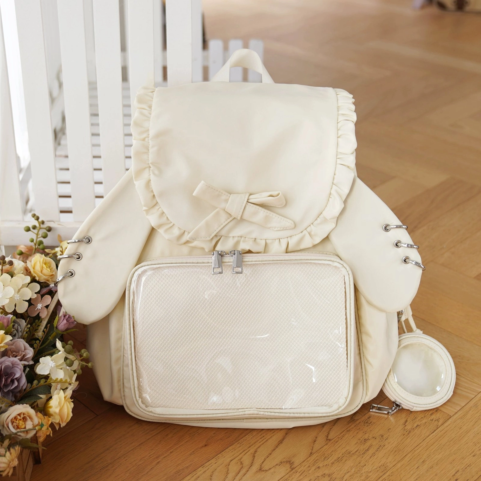 Cream white Jirai Kei kawaii itabag backpack featuring detachable bunny ear accents, transparent display panel, ruffled trim, and white mini accessories