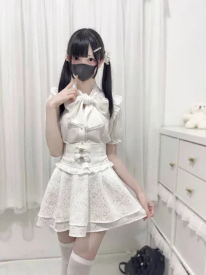 White jirai kei lace bow blouse worn with ruffled skirt and thigh-high socks three-quarter standing front view model bedroom indoor