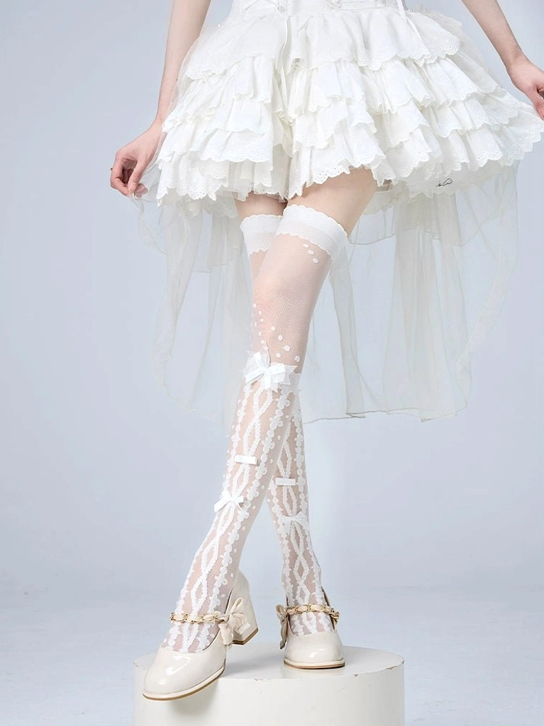 White Jirai Kei over-the-knee socks featuring vine and bow hollow patterns with delicate lace trim, styled on model in white ruffled dress and beige Mary Jane shoes, front low-angle view highlighting sheer mesh construction
