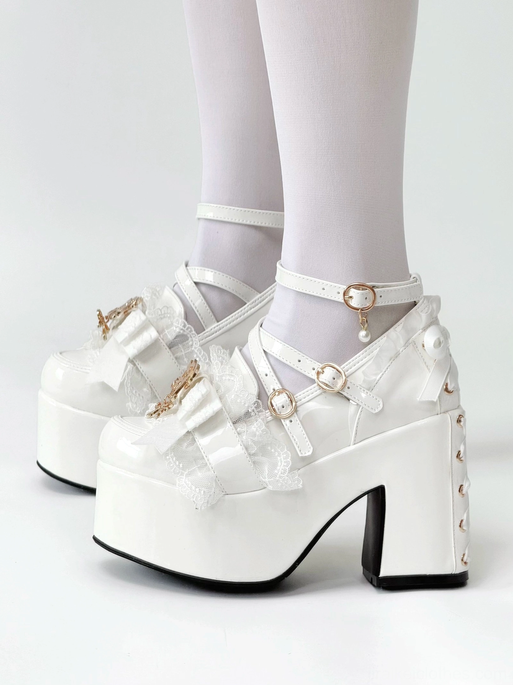 Side view of white patent leather Jirai Kei platform heels being worn with white ankle socks displaying ankle buckle strap bow and lace decorations studded heel