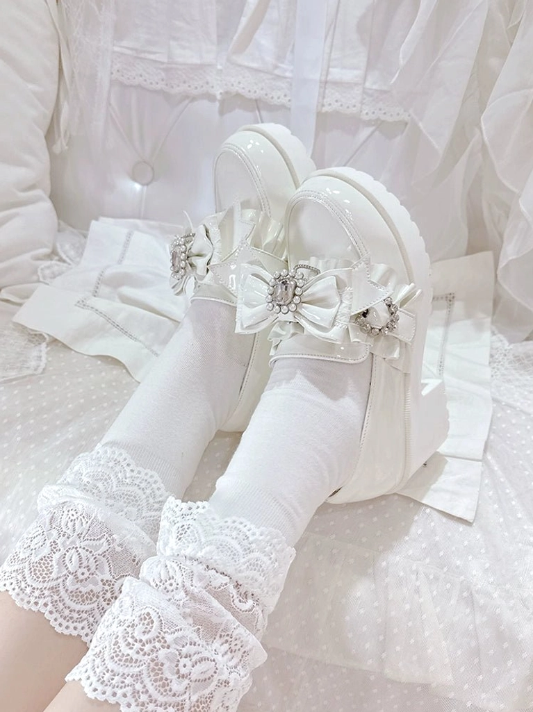 White patent leather Jirai Kei mid-heel loafers detailed product shot showing glossy high-shine finish, rhinestone bow embellishments, ruffled buckle strap and platform heel structure