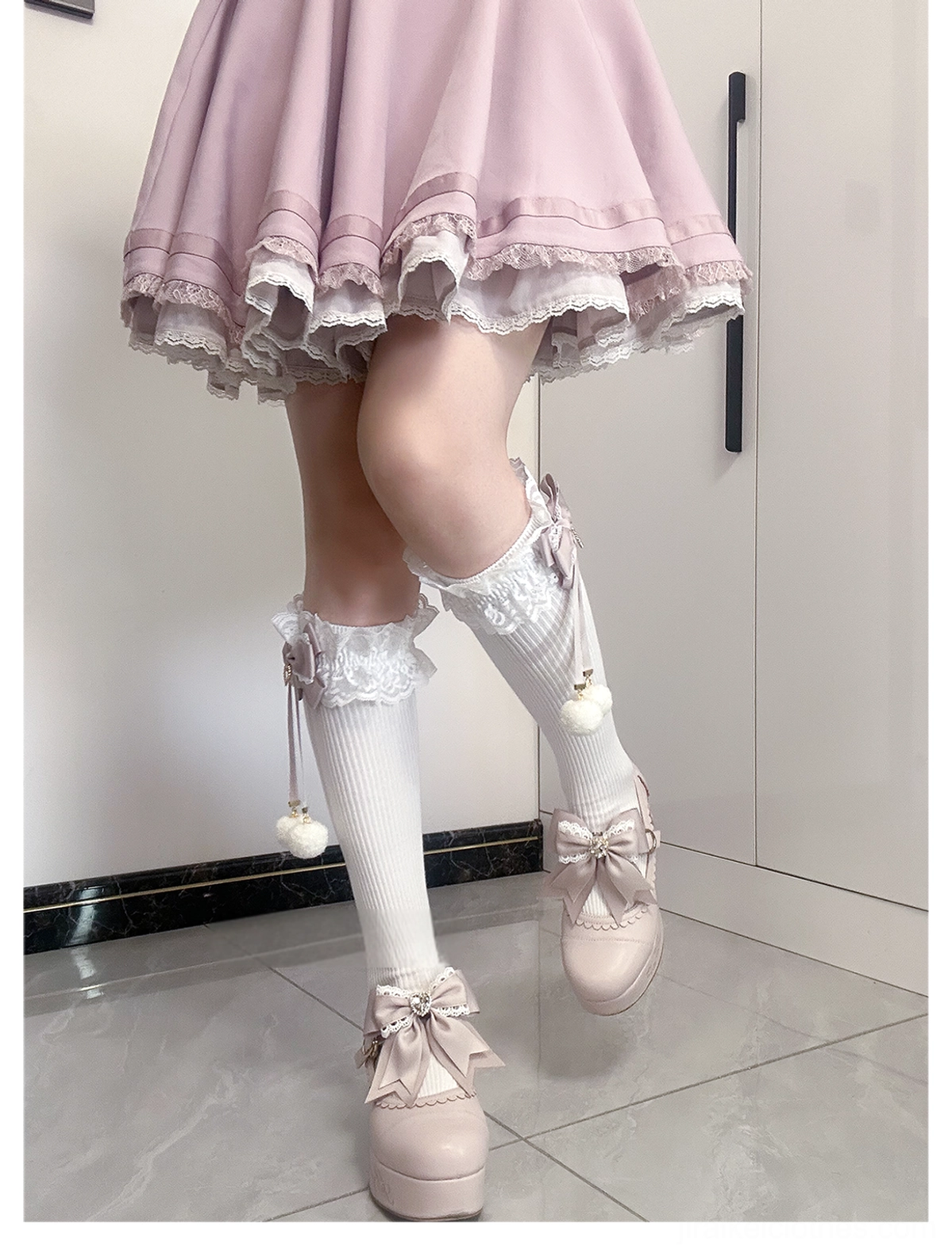 Jirai Kei knee-high socks white-pink colorway flat lay showing full pair lace cuff detail bow accent and hanging pom-poms on white background