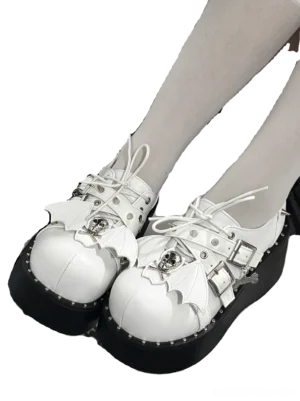 White Jirai Kei platform loafers close-up front view showing black thick sole studded trim and metal bat wing skull decorations