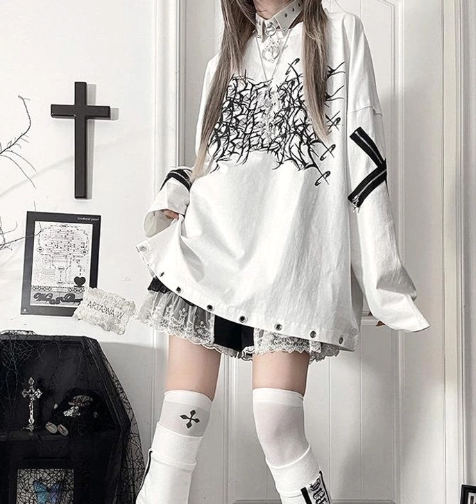 Full-body fashion shot of white jirai kei gothic oversized long-sleeve t-shirt with black thorn cross print, cross strap sleeves, and riveted lace hem in goth room aesthetic