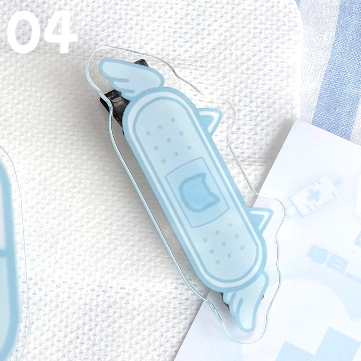 Winged bandage cat face Jirai Kei hair clip with decorative wings acrylic design on white fabric with medical prescription card