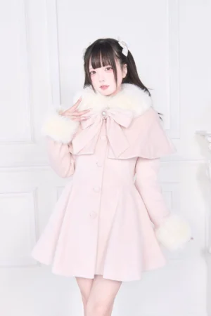 Soft pink Jirai Kei winter coat with white faux fur trims and oversized front bow, front three-quarter view on model with bare legs in white studio setting