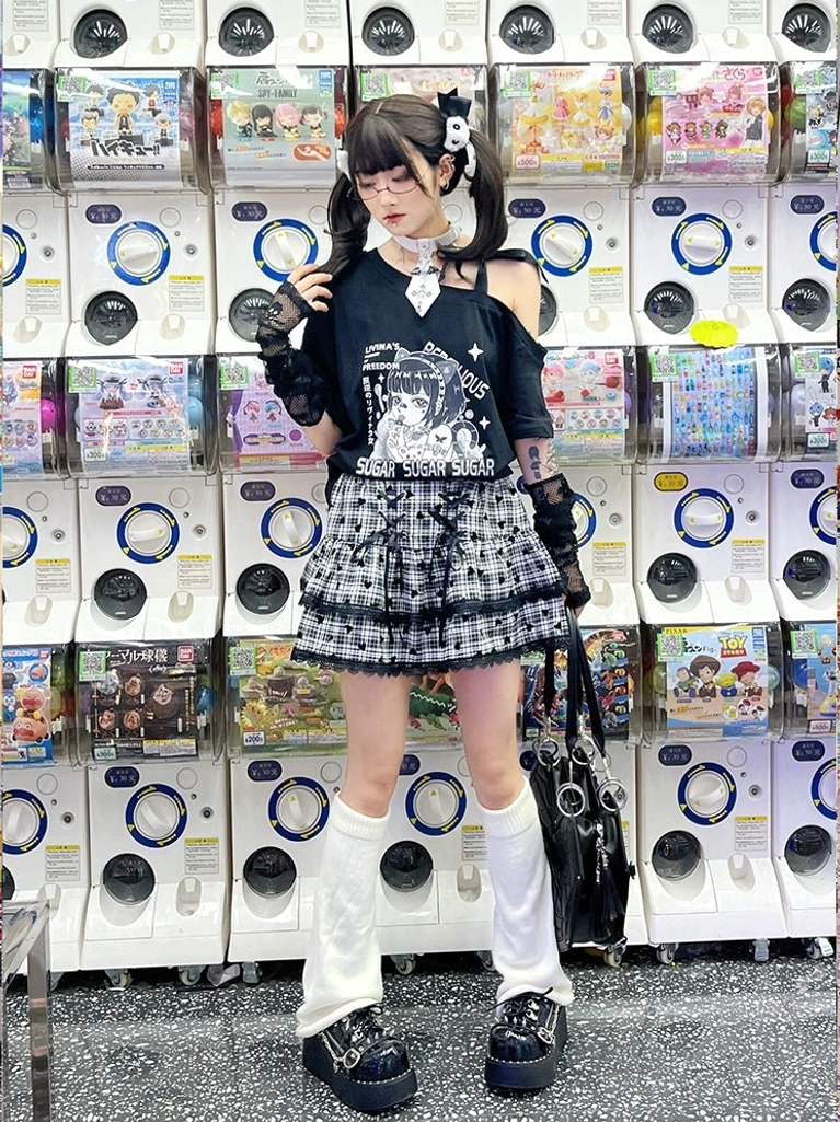 Full-body Y2K Jirai Kei gothic outfit with black off-shoulder tee, black-white plaid mini skirt, white leg warmers, and platform shoes styled in game center arcade setting