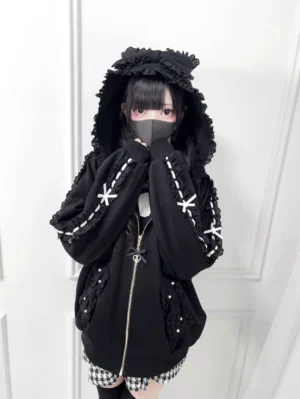 Black Jirai Kei zip-up hoodie with ruffled hood front view, showcasing delicate lace bow sleeve trims and pearl accents, worn by model with dramatic hood raised