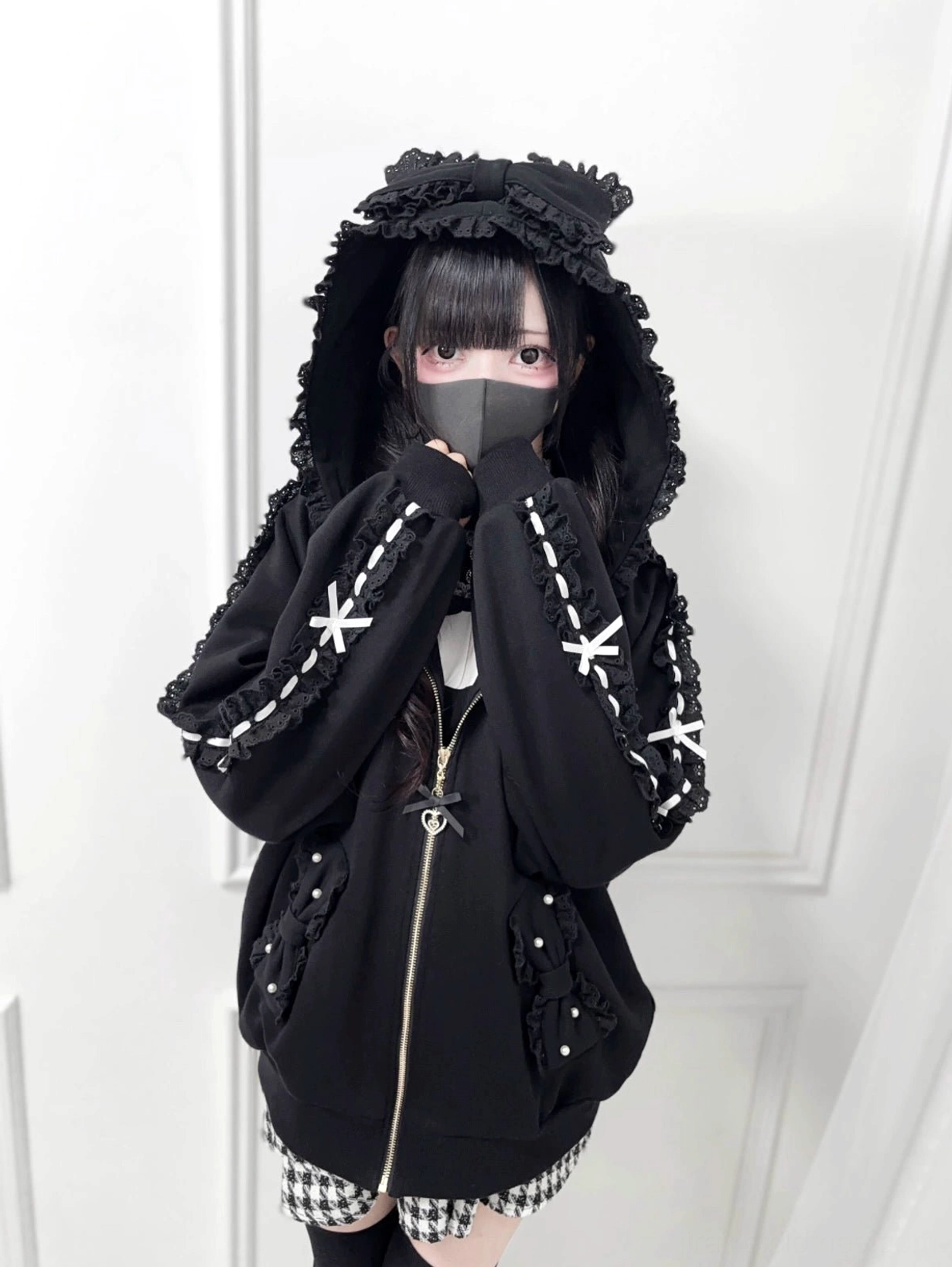 Black Jirai Kei zip-up hoodie with ruffled hood front view, showcasing delicate lace bow sleeve trims and pearl accents, worn by model with dramatic hood raised