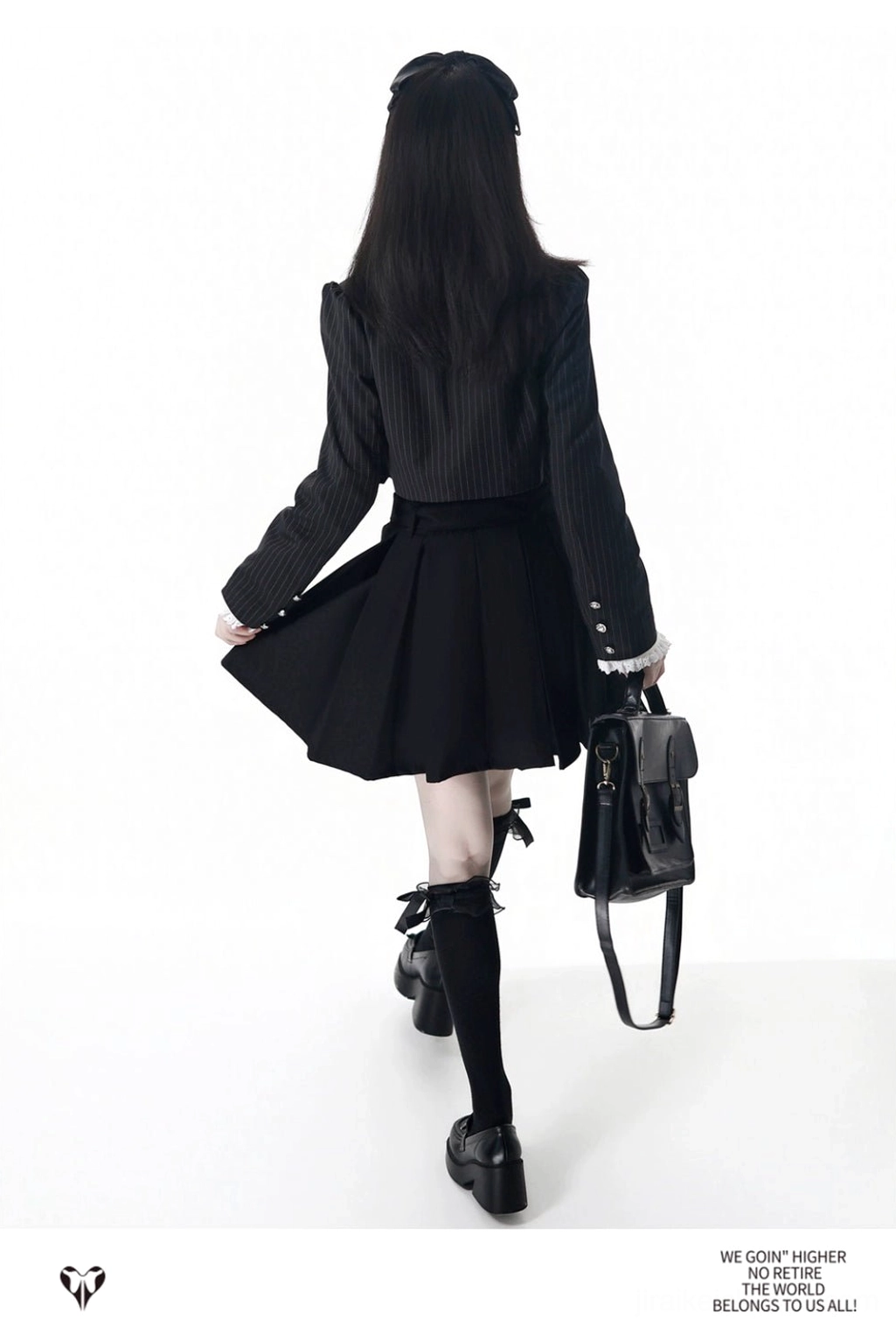 Jirai Kei school uniform back view showing solid black cropped blazer, pinstripe pattern, pleated skirt back shirring, and handbag on female model studio background