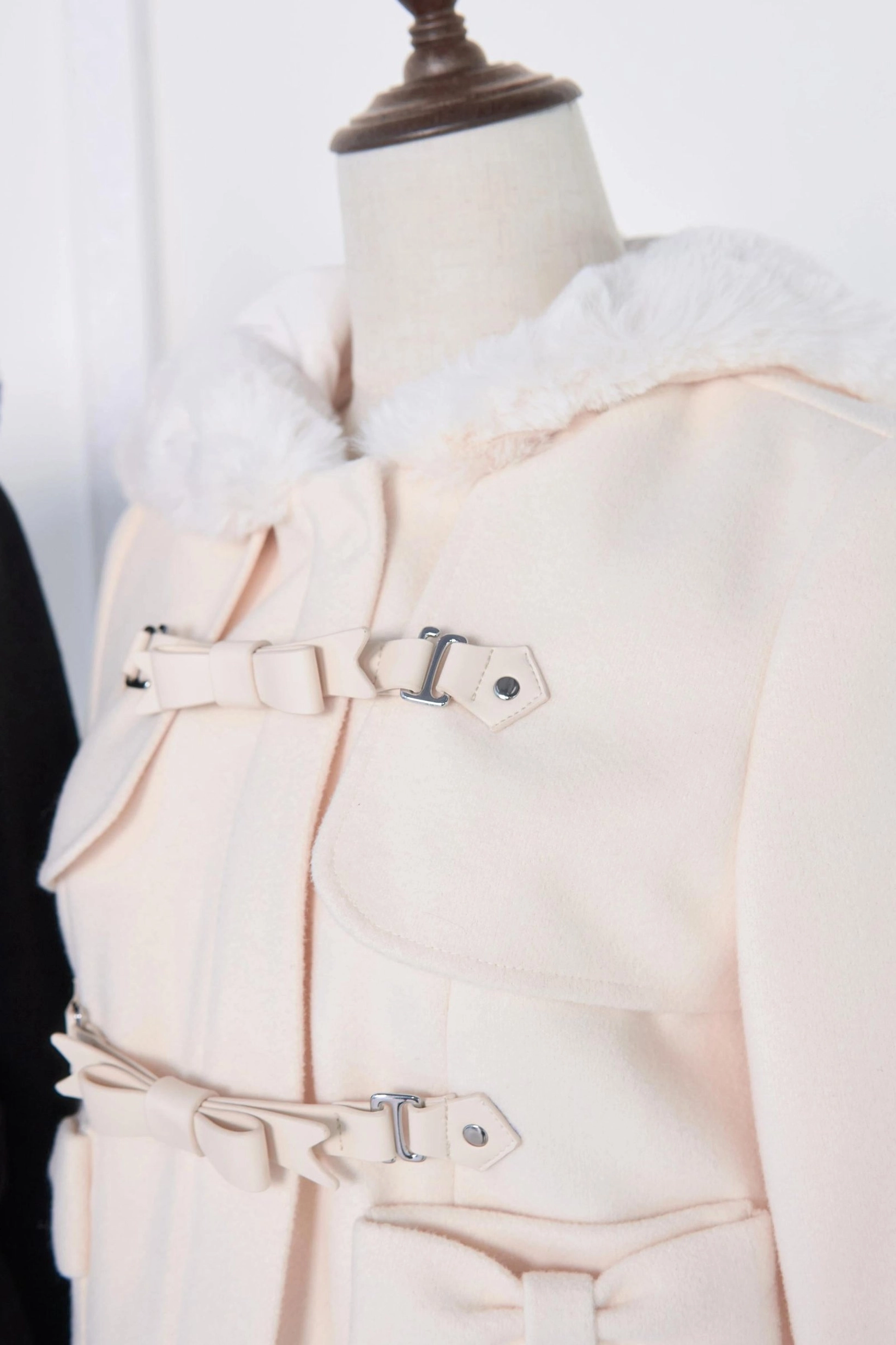 Close-up detail of light apricot beige hooded rousangata coat featuring white fluffy fur collar, light-toned decorative buckle straps, and bow accents on jirai kei coat