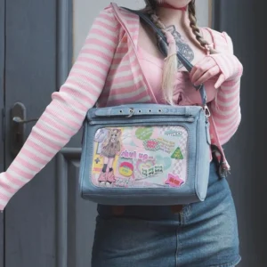 Light blue denim itabag crossbody bag front angle worn with pink striped top and denim skirt, square shape with clear display window showcasing anime sticker decorations