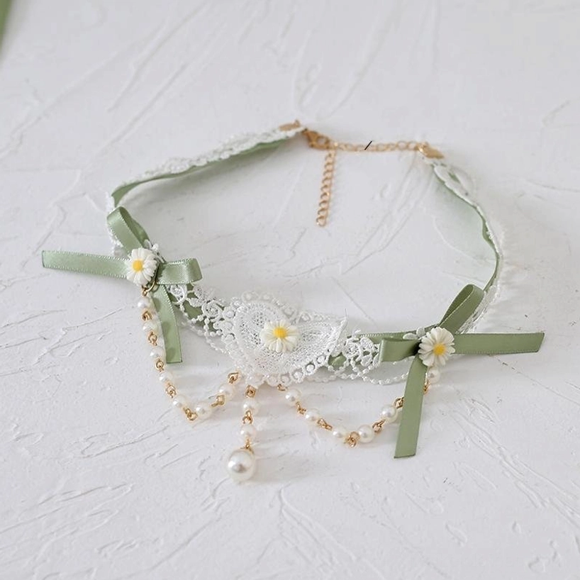 Matcha green lace choker flat lay photography featuring dual decorative bows, daisy flower accents, pearl drop tassel, romantic heart-shaped lace center, on white background—Jirai Kei romantic aesthetic