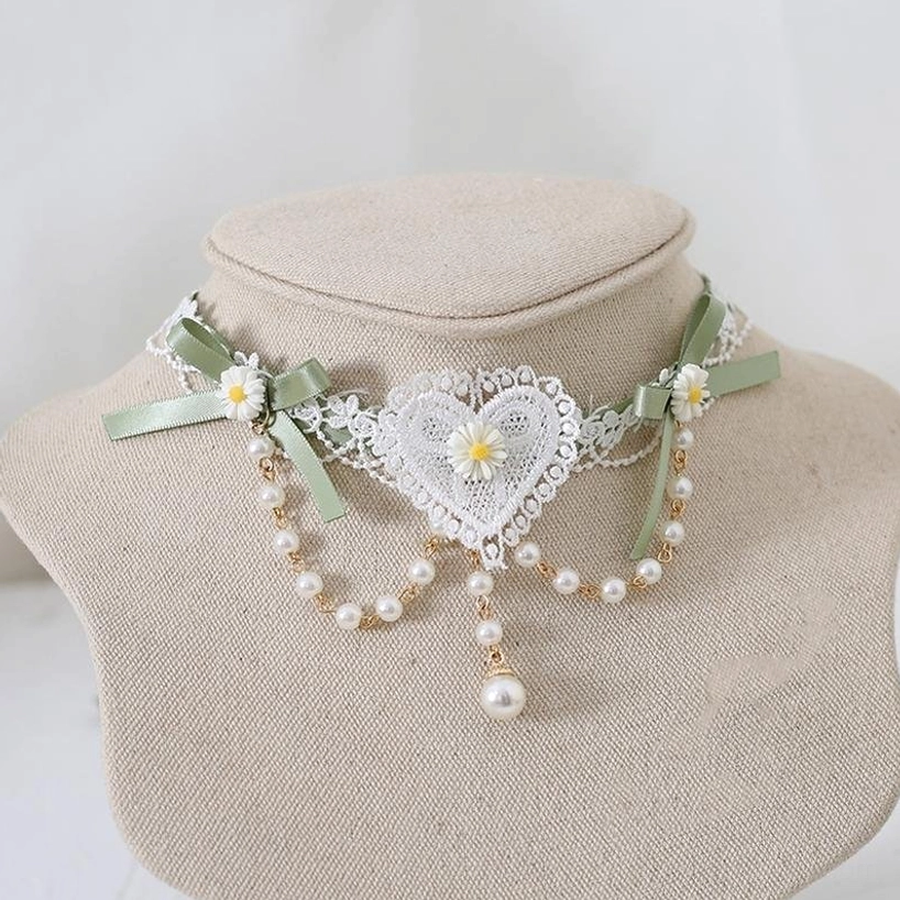 Matcha green Jirai Kei lace choker with white heart details, delicate daisy embellishments, pearl tassel pendant, and gold bead chains—front view on fabric mannequin neck showcasing romantic alternative fashion aesthetic