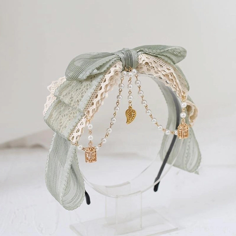 Matcha green Jirai Kei lace headband accessory with ruffled satin bows, beige lace detailing, pearl chain embellishments with gold pendants on acrylic display stand—romantic vintage-inspired headwear