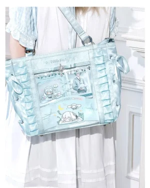 Mint blue jirai kei ita tote bag with rhinestone embellishments and clear display window, worn as crossbody by model in white lolita dress, indoor vintage room aesthetic with ruched satin sides and anime prints