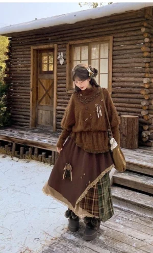 Front three-quarter full-body view of vintage brown Mori Kei sweater with mock collar and asymmetric plaid patchwork skirt, modeled in snowy woodland cabin setting with fuzzy knit details visible