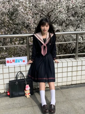 Navy and rose pink Jirai Kei JK uniform outfit front full-body view with classic sailor collar, rose pink bow tie, embroidered pocket details, and high-heat pleated skirt with pink trim shown on model wearing white socks and brown loafers in outdoor cherry blossom setting