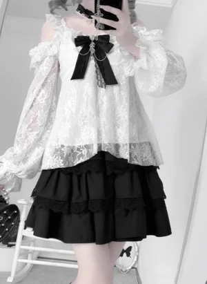 Close-up front view of off-shoulder embroidered lace blouse with detachable chain bow and black tiered rhinestone skirt, indoor home background detail shot