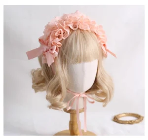 Orange-pink ruffled lace Jirai Kei headband with matching satin bow accents displayed on blonde wig mannequin, front three-quarter angle showcasing warm-toned delicate lace and feminine ribbon tie