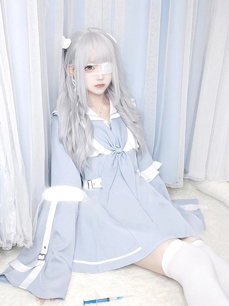 Oversized pastel blue sailor Jirai Kei dress set with white trim, waist belt, strap decorations, and matching shorts worn by long silver-haired model with eye patch in curtained indoor setting