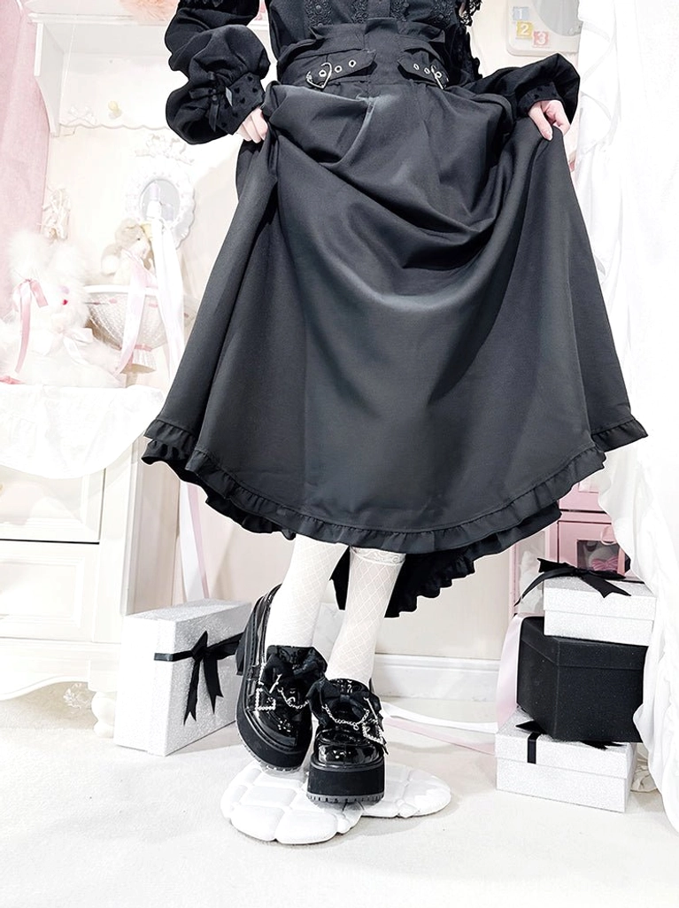 Paired black patent leather Jirai Kei platform shoes front close-up on white display base, showing glossy finish, square rhinestone straps, chunky platform heel, worn with white socks and black high-waisted ruffled skirt