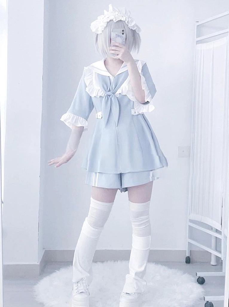 Full-body front shot of pastel blue sailor Jirai Kei outfit featuring ruffled sailor collar, front bow knot, matching shorts, white thigh highs, and frilly headpiece on fluffy rug