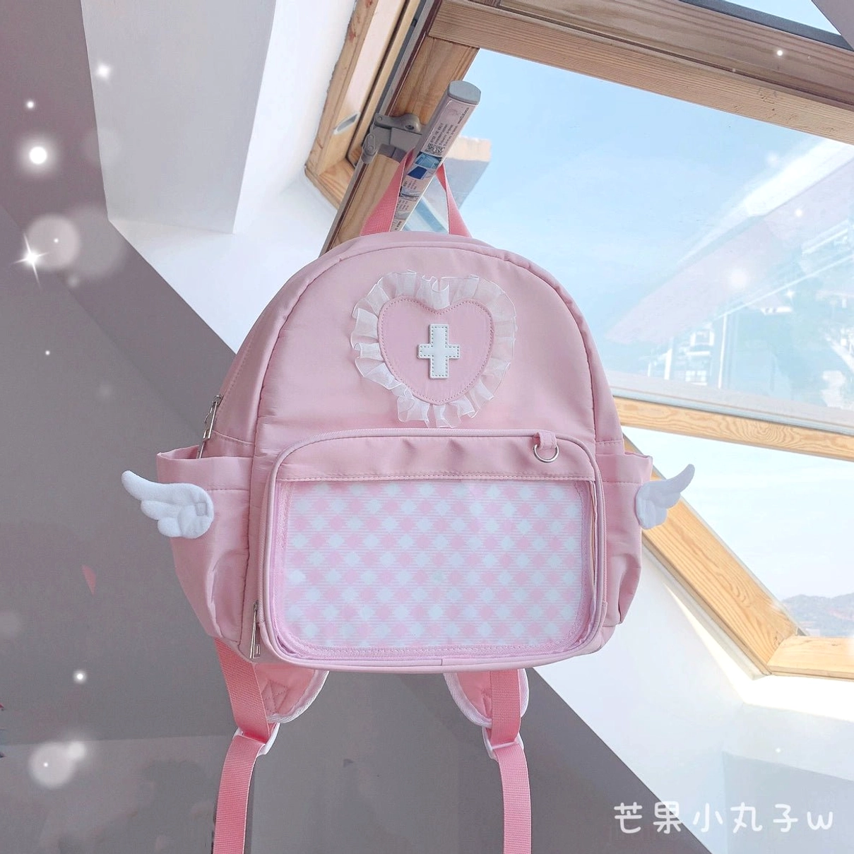 Pink angel-inspired Jirai Kei itabag backpack with heart lace cross ornament, transparent display pocket and elegant angel wing accents for Tenshi fashion enthusiasts