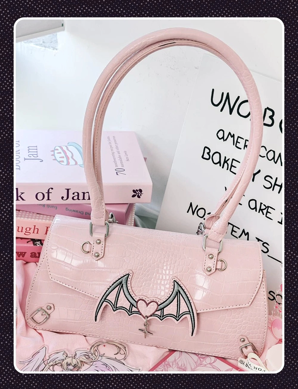 Pink bat-themed croc Jirai Kei handbag with bat-heart embroidery top handle strap front flat lay view on stacked books prop
