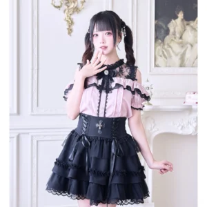 Pink off-shoulder Jirai Kei blouse with black lace hollow-out neckline, rhinestone bow tie, and ruffled chest detail on model wearing twin-tail hairstyle in vintage palace studio setting