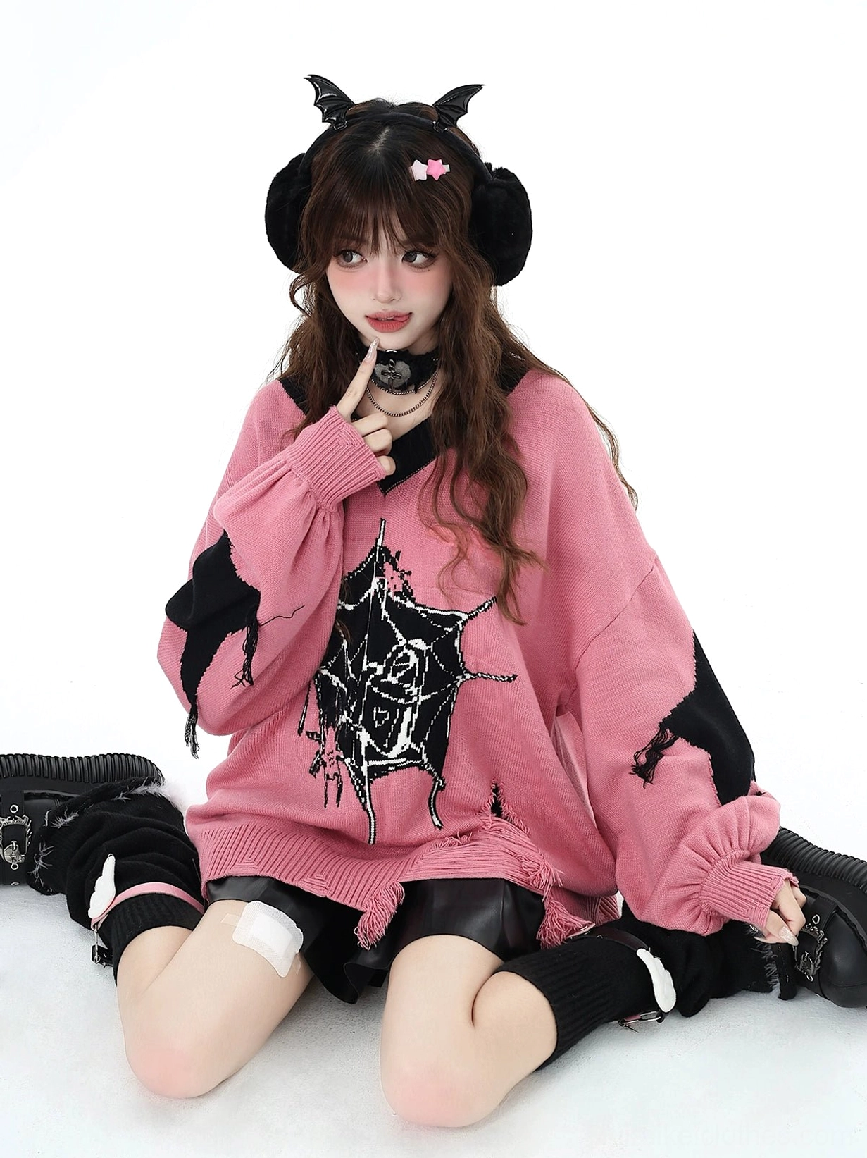 Pink Jirai Kei knit sweater featuring front chest spider print with model posing finger near chin while wearing devil horn earmuffs