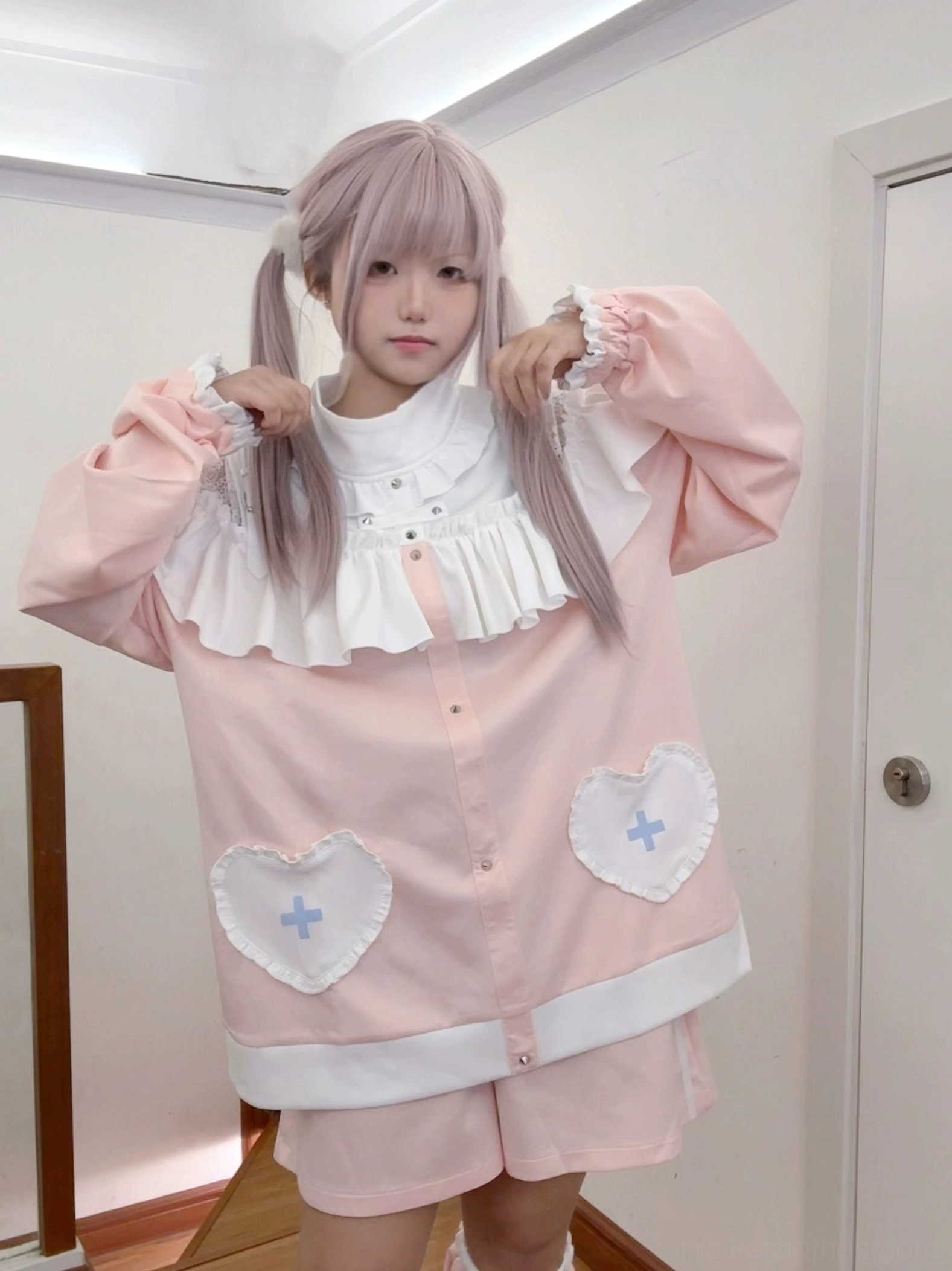 Pink Jirai Kei lolita sweatshirt set full-body front view with puff sleeves and high ruffled collar, hands adjusting sleeves and heart-cross pocket embellishments
